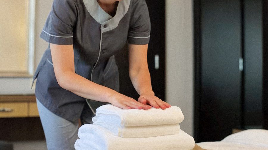 Горничная укладывает полотенца на кровати Стопка полотенец на заправленной кровати